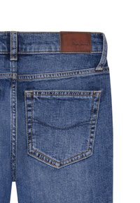 Jeans de mezclilla azul oscuro con una etiqueta de cuero marrón en la cintura, con costuras visibles y un bolsillo trasero decorativo.