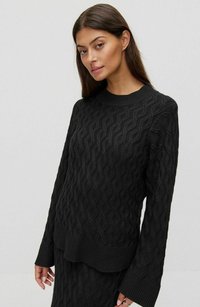 Svart stickad tröja med ett texturerat zigzag-mönster, rund uringning och ribbade ärmslut och nederkant. Strukturerad passform med långa ärmar.
