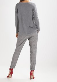 Grauer übergroßer Pullover mit langen Ärmeln, kombiniert mit grauen karierten Hosen und roten High Heels. Weiches Material, lässige Passform, entspannter Stil.