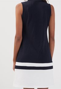 Robe sans manches présentant un haut bleu marine foncé avec une jupe blanche, ornée de rayures horizontales bleu marine et blanches près de l'ourlet.