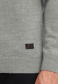 Light gray knitted sweater with ribbed hem, cuff, and small black label reading "Solid Denmark Since 1999" near the wrist and waist.