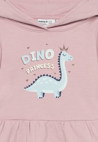 Šviesiai rožinė mažylio džemperis su besišypsančiu mėlynu dinozauru, dėvinčiu karūną, ir užrašu "Dino princesė", apsuptu mažų širdelių.