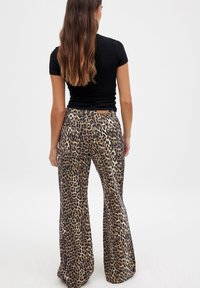 Pantalons évasés en imprimé léopard en tissu doux, dotés d'une taille haute, de poches arrière et d'une texture lisse et brillante. Haut noir non montré.