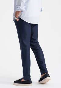 Pantalon bleu marine avec une coupe ajustée, en tissu texturé, associé à des baskets noires dotées d'une semelle de couleur claire.