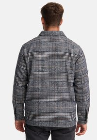 Plaid jacket made of textured fabric in blue, gray, and orange hues. Features a collared neck and long sleeves with buttoned cuffs.