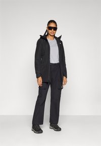 Zwarte waterdichte jas met capuchon, grijs t-shirt, zwarte cargobroek en stevige zwarte wandelschoenen, met een modern ontwerp en praktische details.