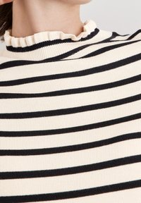 Pull à col roulé à rayures crème et noires, avec une texture côtelée et un col en forme de vagues. Design ajusté avec des rayures horizontales.