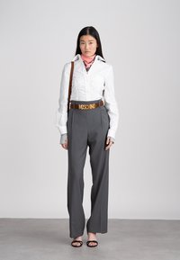 Λευκό, εφαρμοστό πουκάμισο με λεπτομέρειες ρυτίδωσης, συνδυασμένο με ψηλόμεση, γκρι παντελόνα φαρδιάς γραμμής. Καφέ δερμάτινη ζώνη με το λογότυπο "Moschino". Μαύρα σανδάλια.