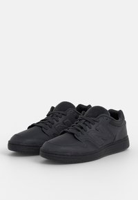 Chaussures de sport noires en cuir avec une texture lisse. Caractéristiques : col rembourré, devant à lacets et logo "N" bien visible.