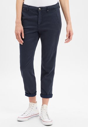 Marineblaue Rollhosen mit glatter Textur, ausgestattet mit frontalen Taschen und einem Knopfverschluss, kombiniert mit weißen High-Top-Sneakers.