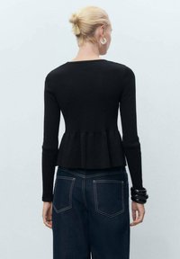 Svart ribbad peplumtop med lång ärm, med en åtsittande midja och en utsvängd fåll. Kombinationen med högmidjade mörka denimjeans.