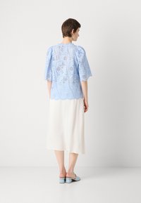 Lichtblauw, kanttop met korte puffmouwen en een gegolfde zoom, gecombineerd met een witte midi-jurk. Blauwe blokhak muiltjes maken de look compleet.