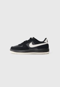 Niske crne Nike tenisice s bijelim swoosh logom i bijelim đonom, prikazane u bočnom profilu na jednostavnoj svijetloj pozadini.