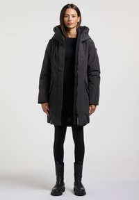 Svart parkas med dragkedja fram, justerbar huva och sidofickor. Har en avslappnad passform och slät textur, i kombination med snygga svarta leggings och stövlar.