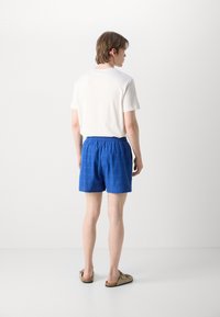 Pantalones cortos azules de tejido texturizado, con cinturilla elástica y un corte relajado, combinados con una camiseta blanca sencilla y sandalias color beige.