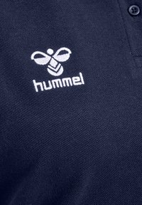 Marinblå pikétröja med en texturerad tygkonstruktion, med en vit broderad logotyp av en bi och ordet "hummel" under. Tvåknapps placket.