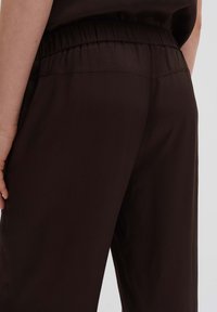 Brown elastic waistband pants with a smooth texture, featuring a relaxed fit and simple stitching details at the back.
