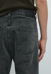 Ciemnoszare dżinsy z denimu o teksturowanym wykończeniu, z czarną skórzaną naszywką na pasku oraz dwoma tylnymi kieszeniami.