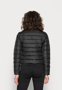 Svart puffjacka med horisontellt kviltat mönster, långa ärmar och en kortad design. Slät, glänsande material utan synlig hårdvara.