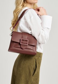 Borsa in pelle bordeaux con un design strutturato, caratterizzata da una grande fibbia rettangolare e da una tracolla rosa a contrasto.