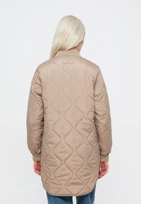 Bežs, quiltots, garš mētelis ar gludu tekstūru, ribinātām piedurknēm un noapaļotu apakšmalu. Audumam ir smalka viļņaina raksts.