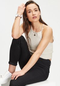 Lichtbeige gebreide crop top met geschulpte randen, gecombineerd met zwarte slim-fit jeans en witte sneakers. Accessoires zijn een horloge en gelaagde kettingen.