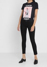 Svart grafisk t-shirt med en hand som håller en cigarett, med texten "GOOD TIMES". Kombinerad med svarta skinny jeans och svarta slip-on skor.