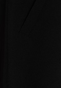 Tissu noir à la texture douce, présentant une coupe droite et un détail subtil de poche intégré au design.