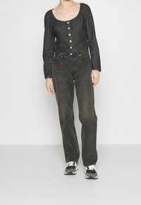 Haut en denim noir à manches longues et col rond, agrémenté de boutons en métal argenté sur le devant. Assorti à un jean sombre taille haute.