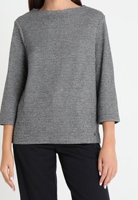 Schwarz-weiß gemusterte Bluse mit Rundhalsausschnitt und Dreiviertelärmeln, die ein kariertes Muster und einen entspannten Schnitt aufweist.