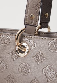 Grå syntetisk håndtaske med præget blomsterdesign og logo, pyntet med guldfarvet hardware og syede stropper.