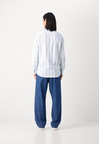 Chemise rayée bleu clair et blanche à manches longues, coupe décontractée. Associée à un pantalon en denim bleu ample. Chaussures de couleur neutre.
