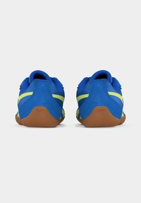 Ζευγάρι μπλε αθλητικά παπούτσια με κίτρινες ρίγες και καφέ σόλες, απεικονιζόμενα από πίσω σε απλό λευκό φόντο.