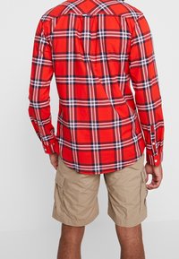 Camicia a quadri rossi con bottoni, che presenta strisce blu navy e bianche. Abbinata a pantaloni cargo beige con tasche laterali.