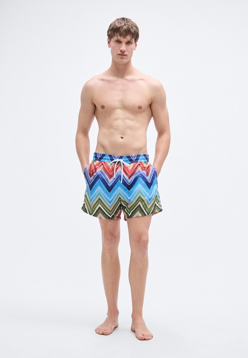 Costume da bagno da uomo con motivo a zigzag colorato in blu, rosso, verde e beige. Realizzato in tessuto leggero con vita elastica.
