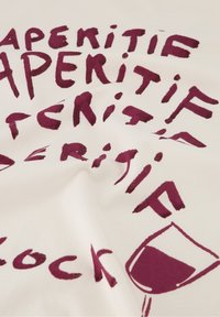 Katoenen stof met een witte achtergrond waar in dikke, bordeauxrode letters het woord "Aperitif" staat. Bevat een afbeelding van een wijnglas.