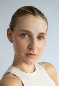 Patch en silicone sur le front d'une personne, présentant un design lisse et translucide. Le fond neutre met en valeur la forme et la texture du produit.