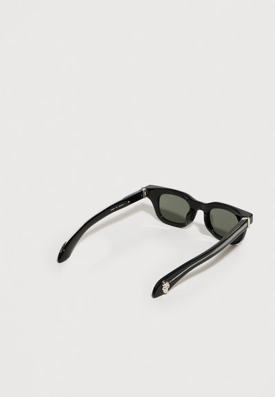 Μαύρα ορθογώνια γυαλιά ηλίου με σκούρους φακούς και γυαλιστερές φαρδιές μπράτσες, ανοιχτά πάνω σε λευκή επιφάνεια.