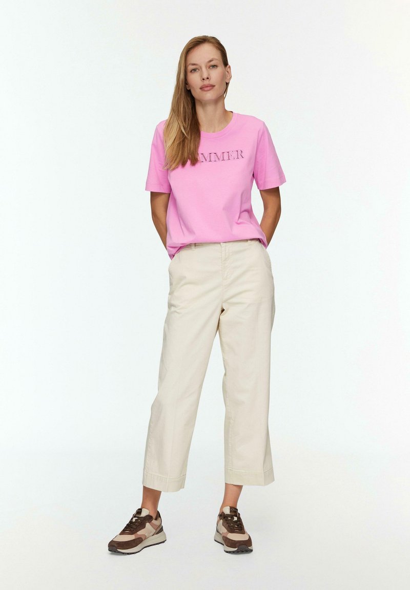 Rosa Baumwoll-T-Shirt mit dem Text "SUMMER", beigefarbene, cropped Hosen und braune sowie beigefarbene Sneaker. Glatte Texturen und lässige Passform.