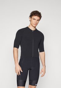 Haut de sport noir à manches courtes avec une fermeture éclair à l'avant, associé à un short noir rayé avec une bande de couleur unie à l'ourlet.