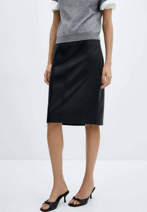 Woman wearing a knee-length black skirt, gray short-sleeve sweater, and black heeled open-toe mule shoes on a plain background.