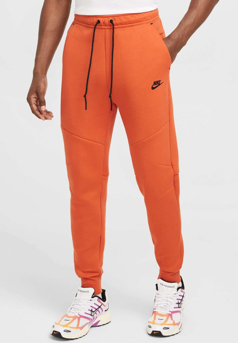 Pantalones jogger naranja con cintura con cordón, acentos negros y bolsillos laterales, confeccionados en una tela suave con un ajuste cónico.
