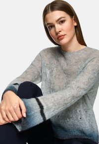 Hellgrauer gestrickter Pullover mit Ombre-Effekt, der komplexe Muster aufweist und eine lockere Passform hat. Weiche Textur mit langen, leicht ausgestellten Ärmeln.