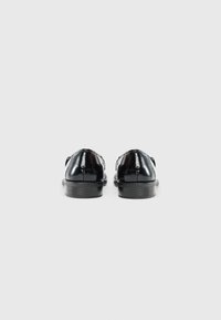 Zapatos de charol negro con una textura suave, puntera redondeada y suelas planas de goma negra, con un diseño minimalista y sin acentos visibles.