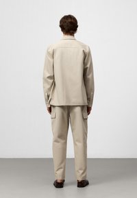 Completo in cotone beige con camicia a maniche lunghe e colletto e pantaloni cargo con tasche laterali. Texture liscia, vestibilità comoda, design informale.