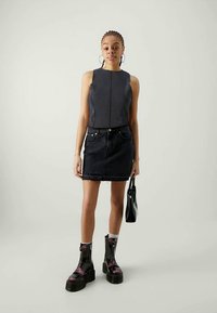 Fustă mini din denim negru, asortată cu un top închis cu dungi. Modelul poartă cizme negre masive cu accente roz și ține o geantă mică neagră.