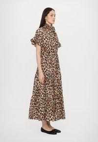 Leopardmønsterkjole i lett stoff. Har volangermuffer, høy krage og tiered skjørt. Fargepalett: beige, brun og svart.