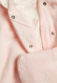 Lichtroze fleece kledingstuk met een bloemen reliëfpatroon. Bevat drukknoopsluitingen en een gelaagd ontwerp met een zachte binnenvoering.
