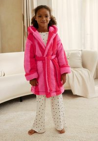 Fuzzy pink robe with contrasting darker pink stripes, a hood, and belt; worn over white pajama pants with small red heart patterns.