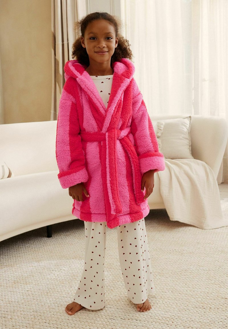 Fuzzy pink robe with contrasting darker pink stripes, a hood, and belt; worn over white pajama pants with small red heart patterns.
